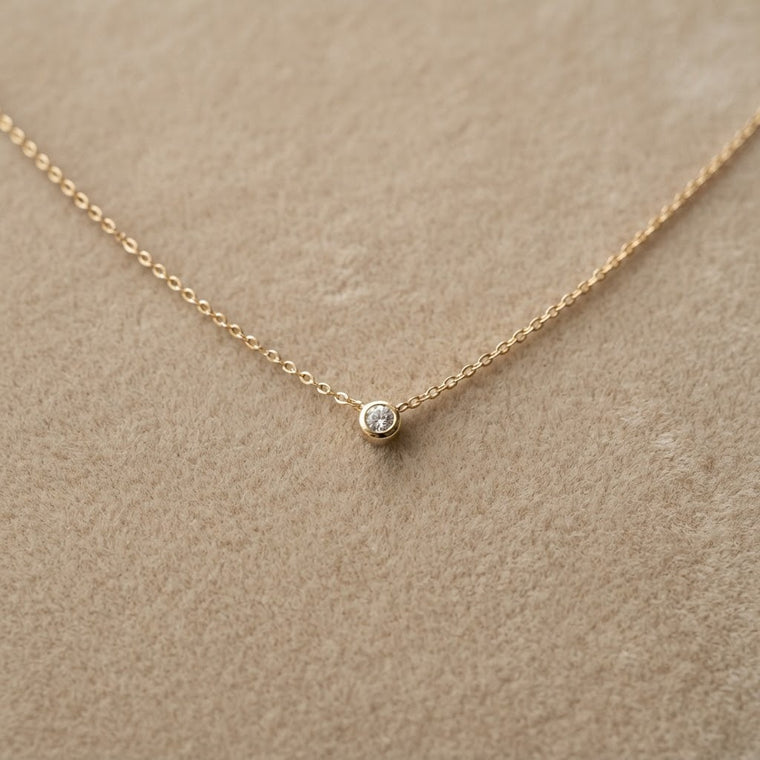 Collier doré photographié sur un fond de velours beige avec beaucoup d’espace autour